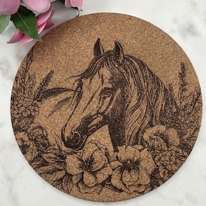Puede incluir: Posavasos redondo de corcho con un grabado de la cabeza de un caballo rodeada de elementos florales. El diseño en tonos marrones crea una estética rústica y natural. Un accesorio decorativo para el hogar.