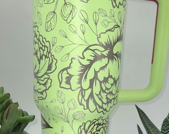 May include: A large, lime green travel mug with a floral design in dark gray. The mug has a handle, a clear lid, and a green top. The mug is approximately 9 inches tall.
