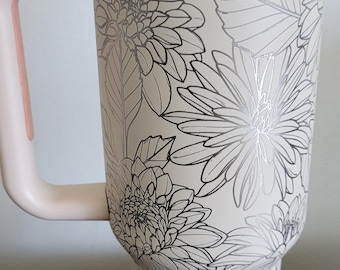 May include: A white insulated tumbler with a floral design in black and silver. The tumbler has a light pink handle and a white lid. The tumbler is approximately 9 inches tall.