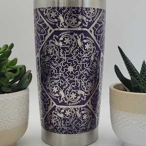May include: A stainless steel tumbler with a purple and silver design. The design features a repeating pattern of flowers, vines, and the words "F*ck Off" and "F*ck It".