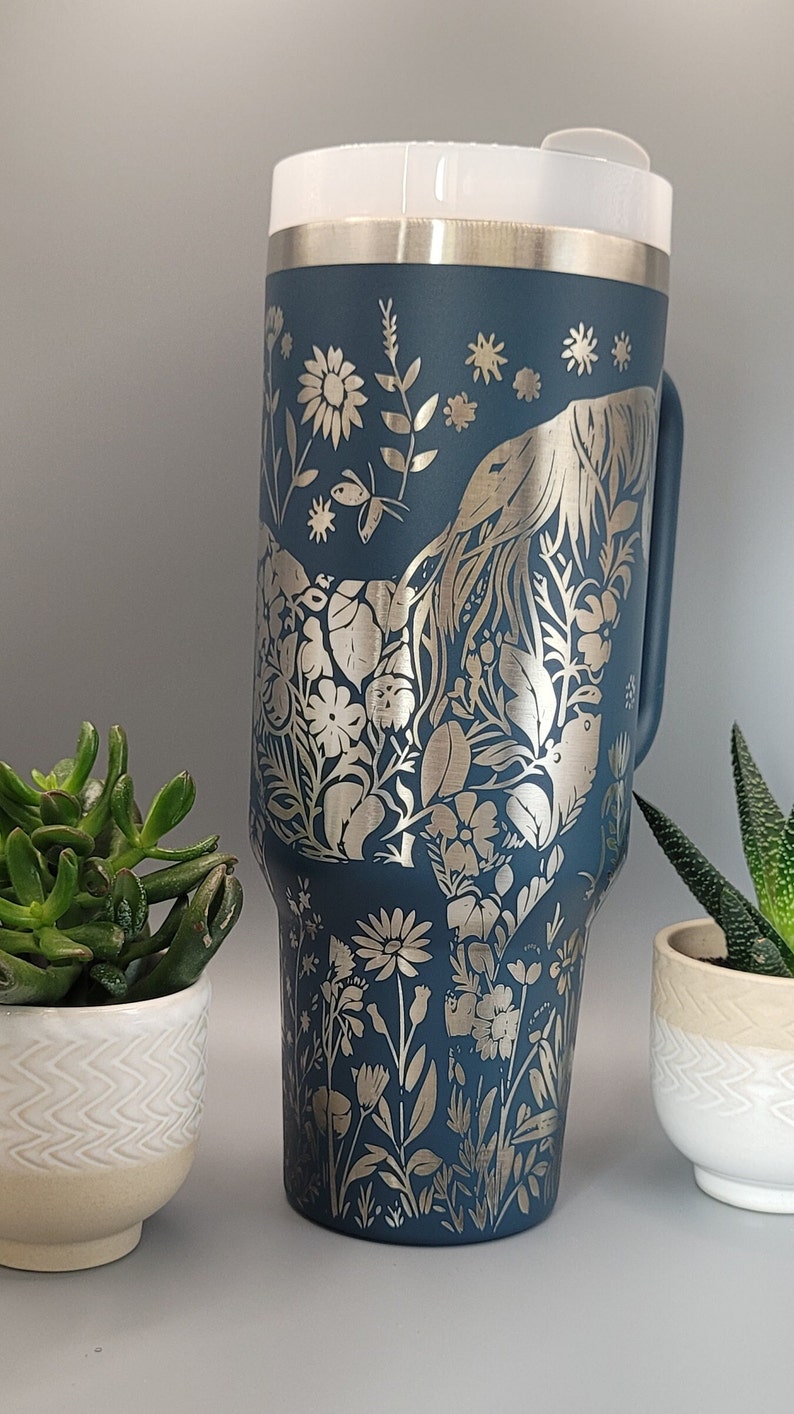 May include: A dark blue stainless steel tumbler with a silver floral design. The design features flowers, leaves, and a bird.