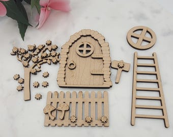 Könnte beinhalten: Eine Sammlung unfertiger Holz-Feengarten-Accessoires. Enthält eine Tür, einen Baum, einen Zaun, eine Leiter, ein Rad, einen Hammer und dekorative Elemente. Ideal für Bastelarbeiten und die Gestaltung von Miniaturlandschaften. Die Teile sind aus Naturholz gefertigt.