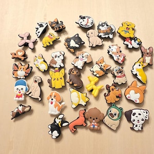 Könnte beinhalten: Eine Sammlung farbenfroher Charms zum Thema Hunde in verschiedenen Rassen und Stilen. Die Charms umfassen eine Vielzahl von Farben, wie Gelb, Braun, Schwarz und Weiß. Einige Charms zeigen Hunde mit Accessoires wie Hüten und Schals.