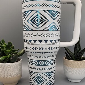 May include: A white travel mug with a blue and white geometric pattern. The mug has a white lid and a white handle.