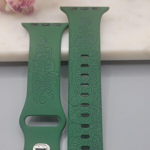 May include: Two green watch straps with floral patterns. The straps are made of a flexible material and feature detailed designs of flowers and leaves. The straps are designed to fit a smartwatch and have a secure clasp.