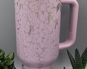 May include: A lavender insulated tumbler with a white lid and handle. The tumbler features a floral design with butterflies. The handle and lid are a matching lavender color. The tumbler is shown with small potted plants.
