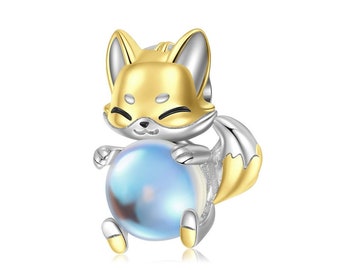 May include: A silver and gold charm featuring a cartoon fox holding a blue iridescent pearl. The fox has a cute expression and a curled tail.