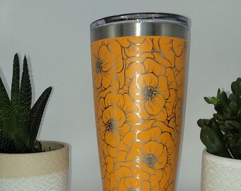 May include: A stainless steel tumbler with a floral design. The tumbler is orange with a silver floral pattern.