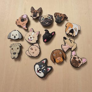 Puede incluir: Una colección de coloridos dijes con temática de perros en varias razas, incluyendo un pug, husky y bulldog. Los dijes están hechos de un material gomoso y están diseñados para ser adheridos a zapatos u otros accesorios.