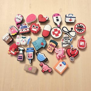 Può includere: Una collezione di ciondoli colorati a tema medico, tra cui uno stetoscopio, un cervello, un cuore, una pillola e camici medici. Altri ciondoli includono una siringa, una mascherina e un cerotto con un cuore.