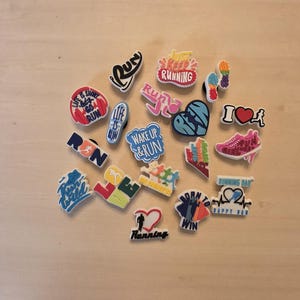 Può includere: Una collezione di ciondoli colorati per scarpe con vari design a tema corsa e testi che includono "Run", "Just Keep Running", "Life is Short Let's Go A Run", "Wake Up & Run", "Run Wild", "I Heart Run", "Running Dad" e "Born to Win".