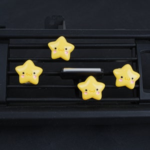 May include: Four yellow star-shaped car air vent clips with cute cartoon faces. Each star has a pink blush and a small smile.