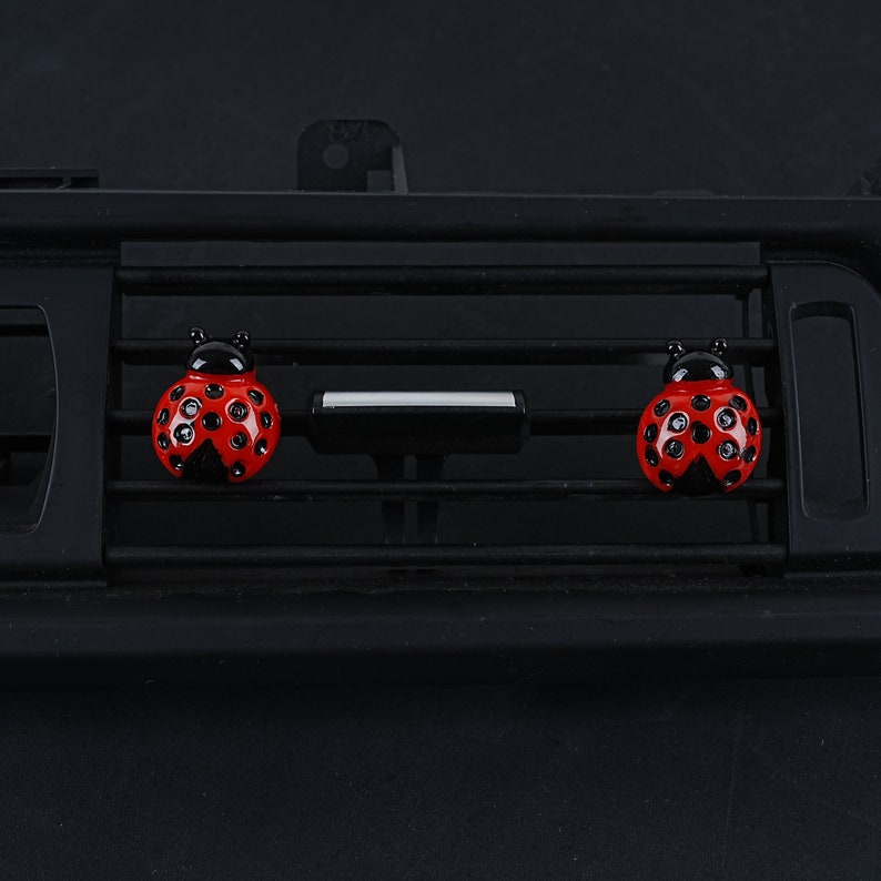 May include: Three red and black ladybug car air freshener ornaments hanging from a black car air vent.
