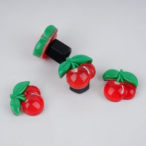 May include: Three red and green cherry-shaped plastic car tire valve stem caps.