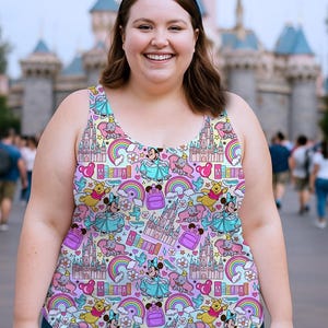 K&ouml;nnte beinhalten: Ein farbenfrohes Tanktop mit einem sich wiederholenden Muster aus Zeichentrickfiguren, Schl&ouml;ssern, Regenbogen und dem Wort "Magical". Das Tanktop wird mit einer blauen Jeans und schwarzen M&auml;useohren getragen. Der Hintergrund zeigt ein Schloss und Menschen.