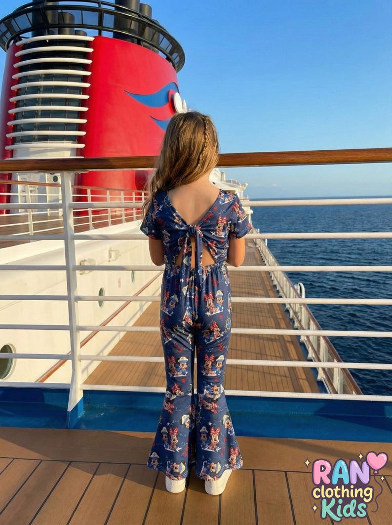 May include: A navy blue jumpsuit with a Minnie Mouse print, featuring a keyhole back and flared legs. The jumpsuit is worn by a person on a cruise ship deck, with the text "RAN clothing Kids" visible.