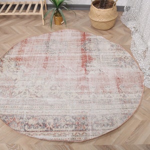 May include: A round area rug featuring a distressed, faded pattern in shades of terracotta orange, muted grey, and cream. The design includes intricate geometric and floral motifs across the surface, finished with a simple bound edge.