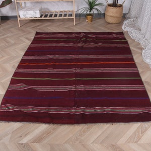 Puede incluir: Una alfombra de rayas color burdeos con detalles en verde, naranja y azul. La alfombra tiene una textura tejida y está hecha de lana.