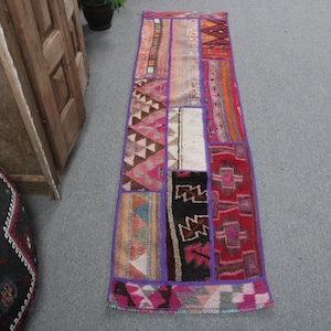 May include: A rectangular patchwork rug with a purple border. The rug features various geometric patterns in shades of pink, red, orange, black, and white. The rug is approximately 60 inches long.