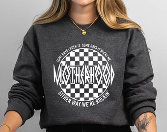 May include: Dark gray sweatshirt with the text "MOTHERHOOD" in a white, stylized font, surrounded by a checkered circle. The text "SOME DAYS I ROCK IT. SOME DAYS IT ROCKS ME. EITHER WAY WE'RE ROCKIN'" is also printed on the sweatshirt.