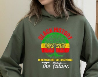 May include: An olive green hoodie with a front pocket and a drawstring hood. The front of the hoodie features a graphic with the words "BLACK HISTORY" above a tree design in red, green, and yellow, with the text "HONORING THE PAST INSPIRING The FUTURE" below.