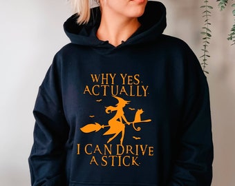 May include: A navy blue hooded sweatshirt with the text "WHY YES, ACTUALLY, I CAN DRIVE A STICK" in orange. The graphic features a witch on a broom with a black cat. The sweatshirt has a front pocket.