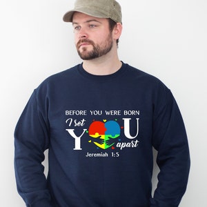 Puede incluir: Sudadera azul marino con un gr&aacute;fico blanco de un coraz&oacute;n hecho de piezas de rompecabezas en rojo, amarillo, azul y verde. El texto "Before you were born I set you apart Jeremiah 1:5" est&aacute; impreso en la sudadera.