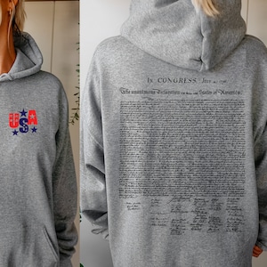 May include: A gray hoodie with a front graphic of "USA" in red and blue. The back of the hoodie features the text of the Declaration of Independence. The hoodie has a hood and a front pocket.