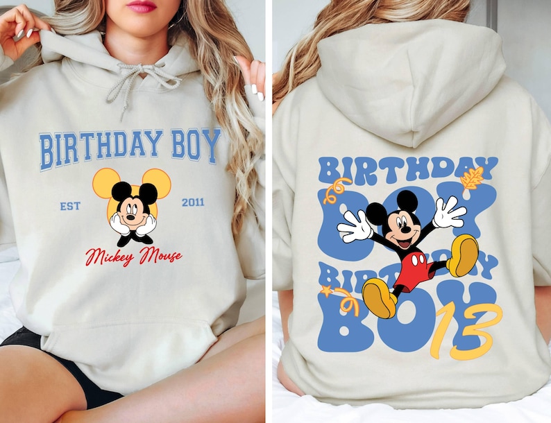 K&ouml;nnte beinhalten: Ein hellgrauer Hoodie mit einem blauen und gelben Mickey Mouse Design. Die Vorderseite des Hoodies sagt "Birthday Boy" mit "Est 2011" und "Mickey Mouse" darunter. Die R&uuml;ckseite des Hoodies sagt "Birthday Boy" in einer blauen und gelben Retro-Schrift mit einer Mickey Mouse Grafik.