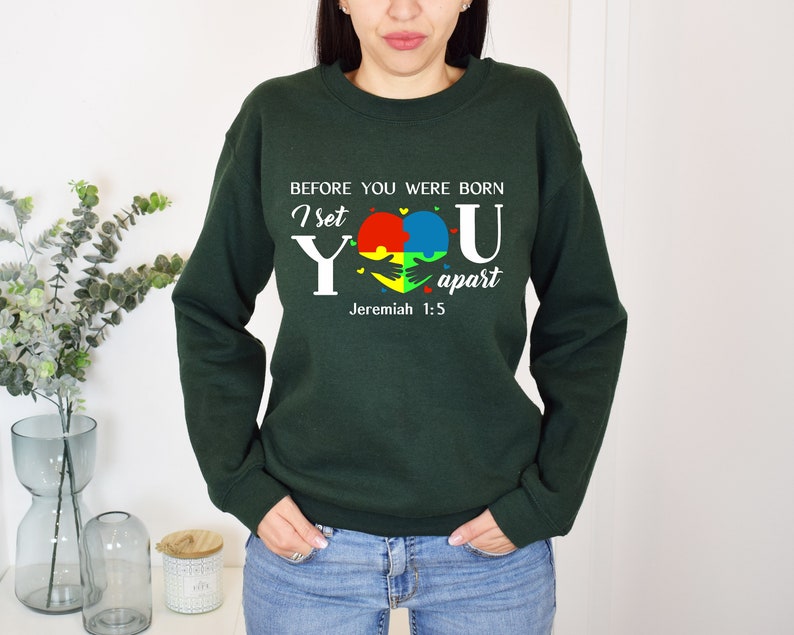 Puede incluir: Sudadera verde con un gr&aacute;fico blanco que dice "Antes de que nacieras, te apart&eacute; Jerem&iacute;as 1:5". El gr&aacute;fico tambi&eacute;n presenta un coraz&oacute;n hecho de piezas de rompecabezas en rojo, amarillo, azul y verde.