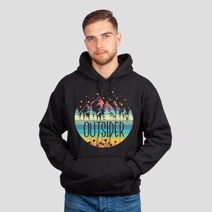 May include: Black hoodie with a colorful graphic of mountains, trees, and the word "OUTSIDER" in a circular design. The hoodie has a front pocket and a hood. The design features pastel colors and stars.