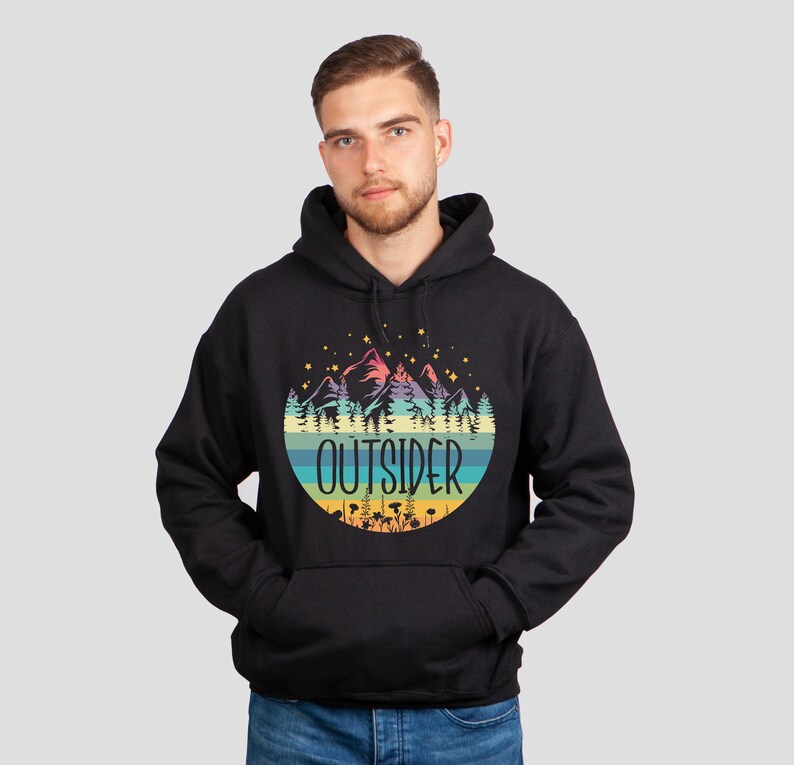 May include: Black hoodie with a colorful graphic of mountains, trees, and the word "OUTSIDER" in a circular design. The hoodie has a front pocket and a hood. The design features pastel colors and stars.