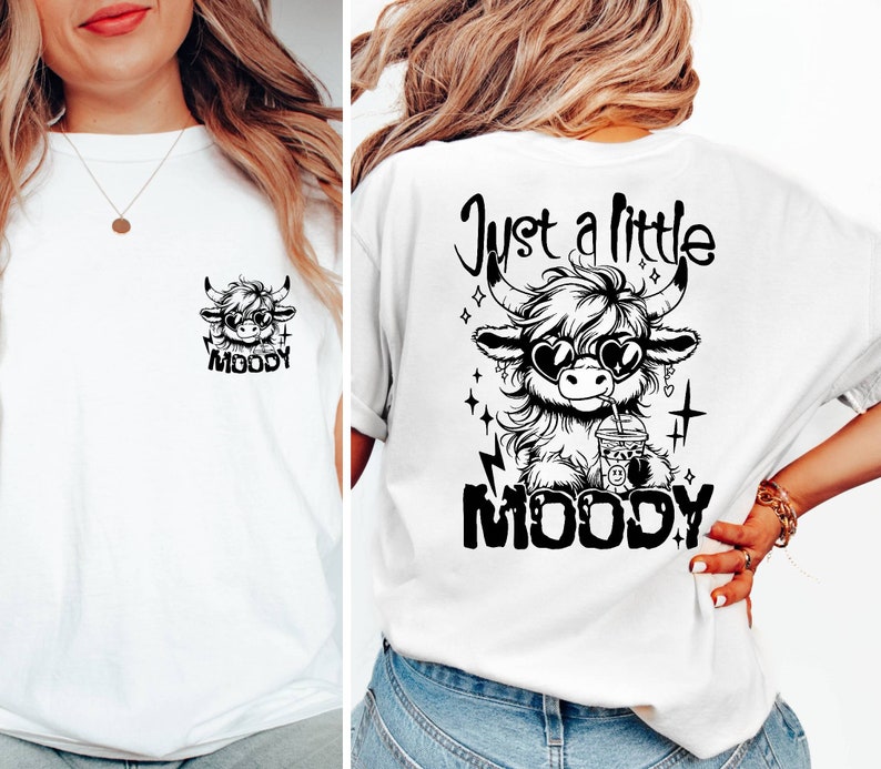 Puede incluir: Camiseta blanca con un gr&aacute;fico en blanco y negro de una vaca de las tierras altas con gafas de sol y bebiendo una bebida. El texto "Just a little moody" est&aacute; por encima de la vaca y la palabra "MOODY" est&aacute; por debajo de la vaca.
