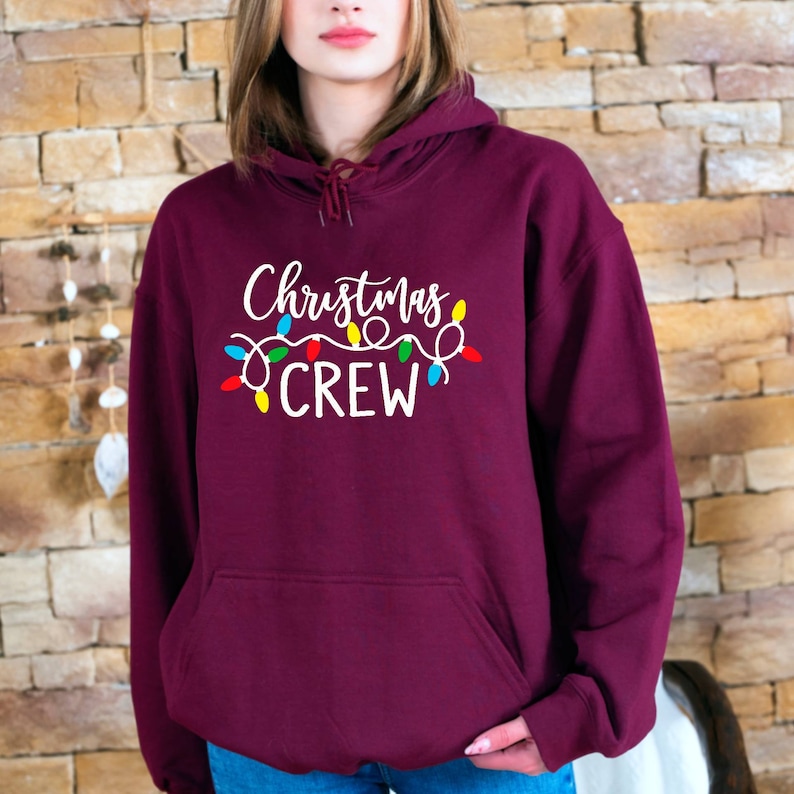 May include: Burgundy hoodie with a white graphic that says "Christmas Crew" with colourful string lights.
