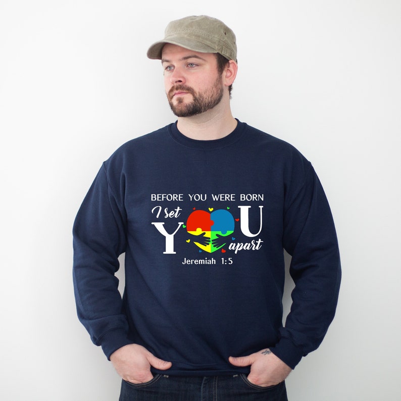 Puede incluir: Sudadera azul marino con un gr&aacute;fico blanco de un coraz&oacute;n hecho de piezas de rompecabezas en rojo, amarillo, azul y verde. El texto "Before you were born I set you apart Jeremiah 1:5" est&aacute; impreso en la sudadera.