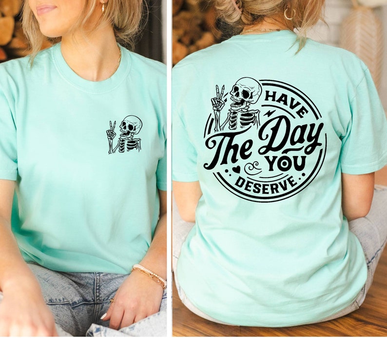 May include: A light blue t-shirt with a skeleton graphic on the front and a circular graphic on the back that says "Have the Day You Deserve" with a skeleton graphic inside the circle.
