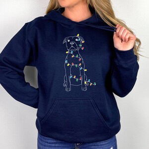 May include: A navy blue hoodie with a white outline of a dog wearing Christmas lights. The dog is sitting and looking forward.