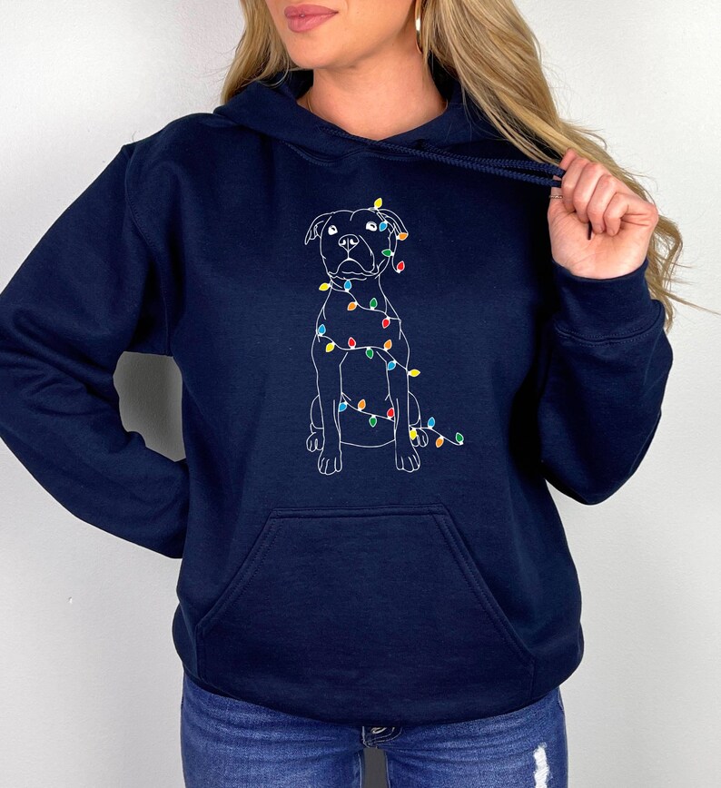 May include: A navy blue hoodie with a white outline of a dog wearing Christmas lights. The dog is sitting and looking forward.