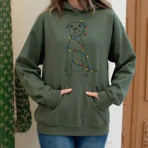 May include: A green hooded sweatshirt with a black and white illustration of a dog wearing Christmas lights. The dog is sitting and looking to the right.