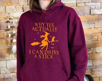 May include: Burgundy hooded sweatshirt with a front pocket and orange graphic. The graphic features a witch on a broom with a cat and the text "WHY YES, ACTUALLY, I CAN DRIVE A STICK."