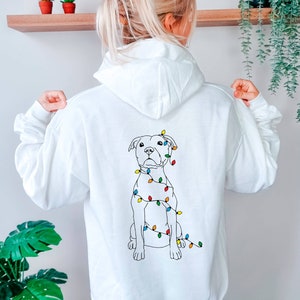 May include: White hoodie with a black line drawing of a dog wearing Christmas lights on the back.