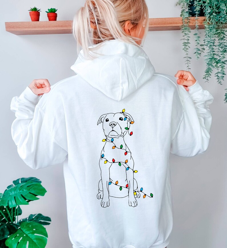 May include: White hoodie with a black line drawing of a dog wearing Christmas lights on the back.