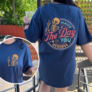 May include: A navy blue t-shirt with a skeleton graphic and the text "Have the Day You Deserve".