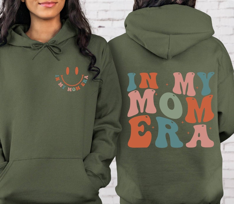 May include: A green hoodie with a smiley face and the text "In My Mom Era" on the front and the text "In My Mom Era" in colorful letters on the back.