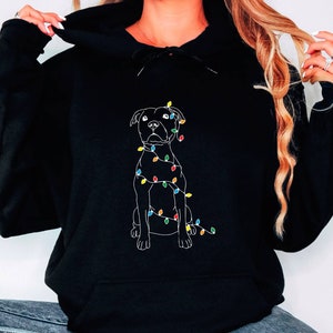 May include: Black hoodie with a white outline of a dog wrapped in Christmas lights. The lights are multi-colored.