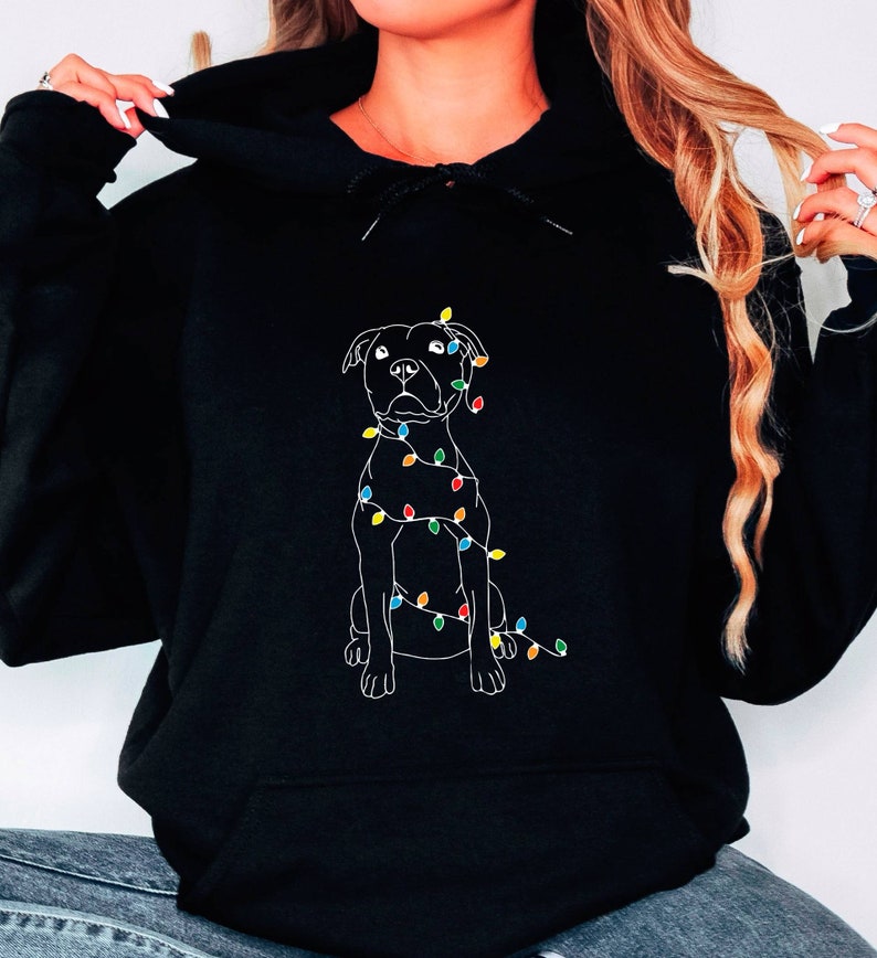 May include: Black hoodie with a white outline of a dog wrapped in Christmas lights. The lights are multi-colored.
