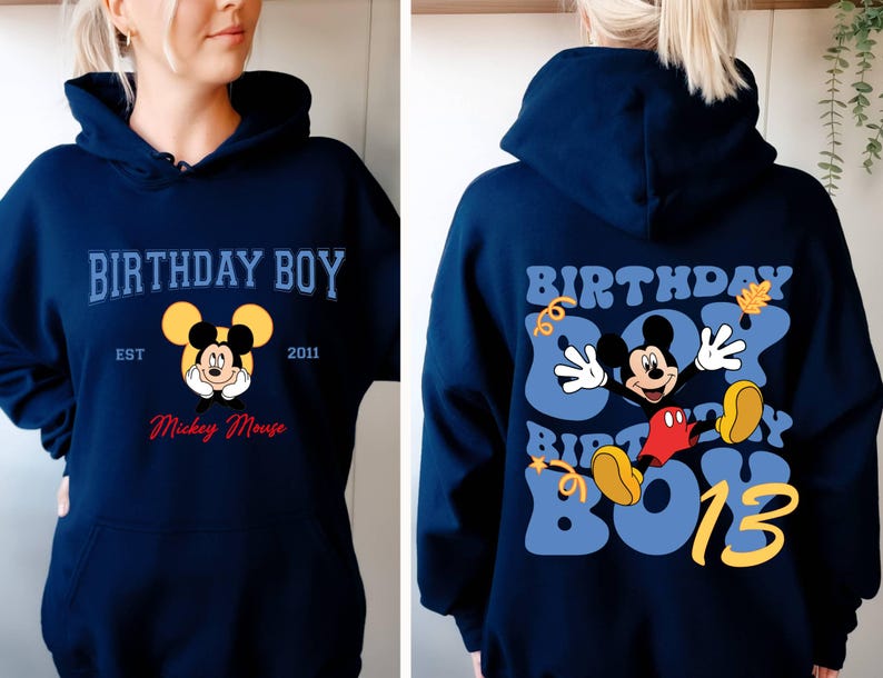 K&ouml;nnte beinhalten: Ein marineblauer Hoodie mit einem Mickey-Mouse-Motiv und dem Text "Birthday Boy Est 2011 Mickey Mouse" auf der Vorderseite. Die R&uuml;ckseite des Hoodies zeigt ein gr&ouml;&szlig;eres Mickey-Mouse-Motiv mit dem Text "Birthday Boy 13" in einer Retro-Schrift.