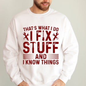 May include: White sweatshirt with a red graphic that says "That's what I do I fix stuff and I know things". The graphic includes a wrench, hammer, and screwdriver.
