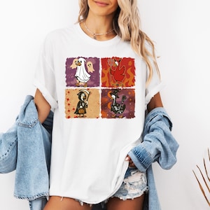 May include: White t-shirt featuring four Halloween-themed chicken illustrations. Each chicken is dressed as a different character: a ghost, a devil, a grim reaper, and a witch. The illustrations are in colorful squares.