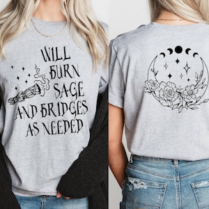 May include: Gray t-shirt with the text "Will burn sage and bridges as needed" on the front and a crescent moon with stars and flowers on the back.